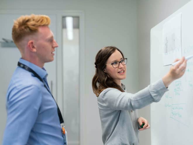 Woman showing man something on a white board